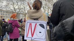 Weine Frau trägt ein Schild mit der Aufschrift NO auf dem Rücken - das O ist dabei erinnnert an Hitlers Konterfei.