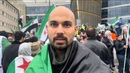 Rashad Lou Lou auf einer Demo im Hintergrund syrische Flaggen 