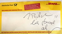 Ein gelber Abholzettel der Deutschen Post mit der handschriftlichen Bemerkung, wo das Päckchen abgegeben wurde