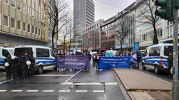 Demonstrierende laufen durch eine Straße mit Antisemitismus Bannern in den Händen, an der Seite stehen Polizisten