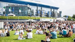 Fans sitzen auf der Wiese vor der Veltins-Arena