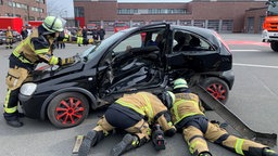 Feuerwehranwährter stehen und liegen an einem Autowrack. Sie üben, wie man eingeklemmte Menschen am besten befreit.