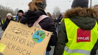 Person in Verdi-Weste und Klimaaktivistin mit einem Schild: Die Erde kocht vor Wut- ich auch