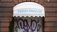 Fenster eines Frieseursalons mit heruntergelassener Rollade