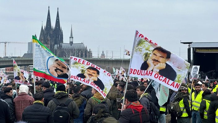 Demonstranten halten Fahnen mit Bildern von PKK-Chef Öcalan. Im Hintergrund ist der Dom zu sehen.