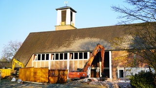 Bagger und Container stehen vor der bereits teils eingerissenen Fassade der Kirche. Dahinter: Der Glockenturm. 