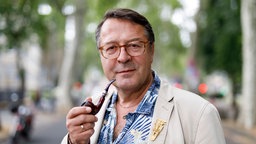 Hans Mörtter, Pfarrer im Ruhestand an der evangelischen Lutherkircher in der Südstadt in Köln, mit einer Pfeife in der Hand.