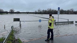 Ein Feuerwehrmann steht in Warendorf von einem überschwemmten Parkplatz.