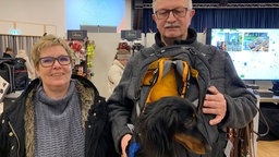 Zwei Hundebesitzer auf dem Hundeweihnachtsmarkt in Bad Sassendorf und ihr Hund, der in einem Rucksack ist.