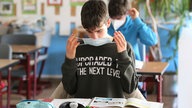 Zwei Schüler mit Mund-Nase-Masken sitzen hintereinander in Klassenraum.