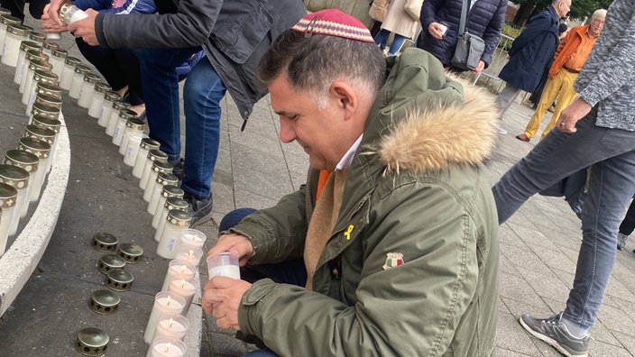 Ein Mann stellt eine Kerze vor der Düsseldorfer Synagoge auf.