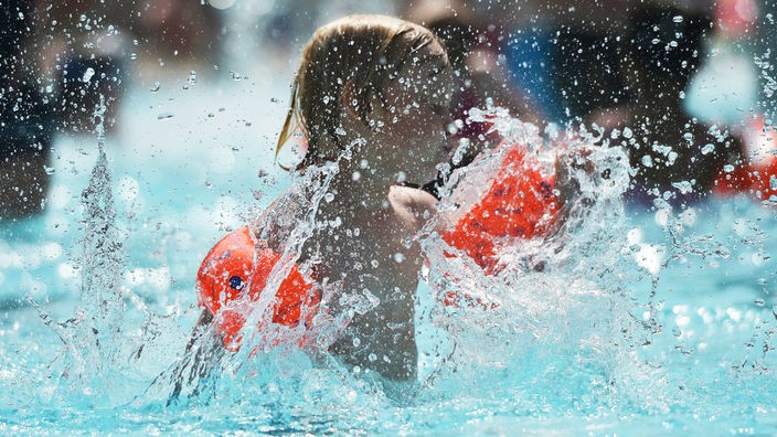 Einer junger Badegast mit Schwimmflügeln kühlt sich hohen Temperaturen in einem Schwimmbad ab.