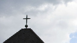 Wolkenverhangener Himmel zeigt sich über einem Kreuz einer katholischen Kirche.