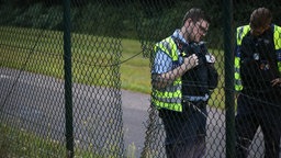 Einsatzkräfte der Polizei stehen neben einem Loch im Zaun am Flughafen Köln/Bonn. Klimaaktivisten haben am Flughafen Köln/Bonn eine Unterbrechung des Flugverkehrs verursacht