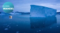 Ein kleines Boot schwimmt während der Abenddämmerung inmitten eines Eisbergfeldes in Grönland