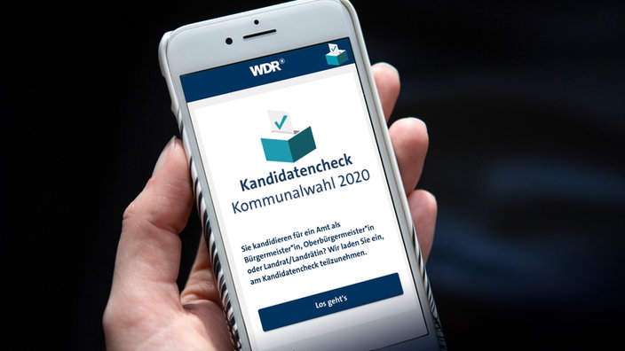 Nahaufnahme von Hand, die Smartphone hält. Bilderschirm ist sichtbar und zeigt Startbild der Kandidaten-Check-App.