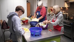 Ein Junge uns zwei Ehrenamtliche stehen in der Küche und bereiten das Mittagessen vor