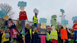 Demonstrierende halten selbstgebaute Puppen mit Sprüchen gegen Sozialkürzungen in die Höhe