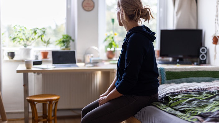 Weibliche Jugendliche sitzt alleine auf dem Bett und schaut zum Fenster