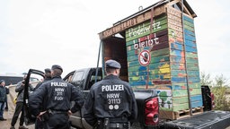 07.10.2018, Nordrhein-Westfalen, Kerpen: Einsatzkräfte der Polizei stehen neben einem auf einen Wagen geladenen Bretterhaus aus dem Hambacher Forst. Das Haus kommt nun ins Museum. Das Bonner Haus der Geschichte baut seine Dauerausstellung um.