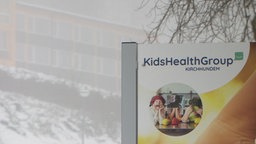 Im Vordergrund Schild der Kids Health Group, im Hintergrund verschneit die geschlossene Reha-Klinik