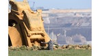 Ein Mann sitze vor einem Schauffelradbagger, hat die Arme weit ausgebreitet, im Hintergrund ist ein Braunkohletagebau zu sehen