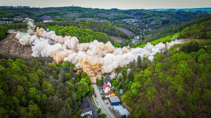 Blick ins Rahmedetal: Nach der Sprengung der maroden Autobahnbrücke liegt eine dicke Staubwolke über dem Tal, eingerahmt von viel Grün der umliegenden Wälder.