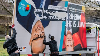 Zwei große Wahlplakate von Friedrich Merz und Olaf Scholz, die von zwei Arbeitern auf dem Kof stehend auf einen Laster verladen werden