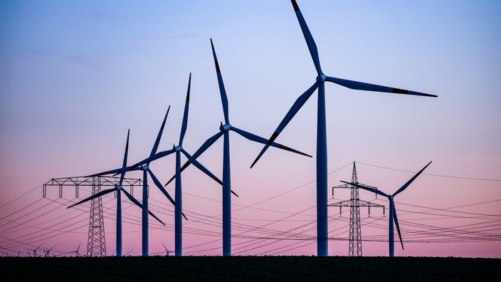 ARCHIV - 04.10.2022, Sachsen-Anhalt, Leuna: Windkraftanlagen und Hochspannungsleitungen sind vor dem Abendhimmel bei Leuna zu sehen. (Zu dpa «50Hertz-Chef Kapferer sieht abnehmenden Widerstand gegen Windenergie»)