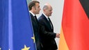 Olaf Scholz und Emmanuel Macron zwischen einer EU- und Deutschland-Flagge.