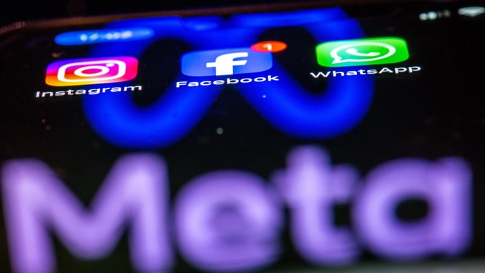 Die Apps Instagram, Facebook und WhatsApp sind auf dem Display eines Smartphones zu sehen, indem sich das Logo des Internetkonzerns Meta spiegelt