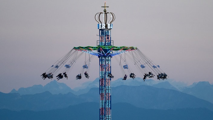 Besucher des Oktoberfests in München fahren mit einem Kettenkarussell. Im Hintergrund sind die Alpen zu sehen.