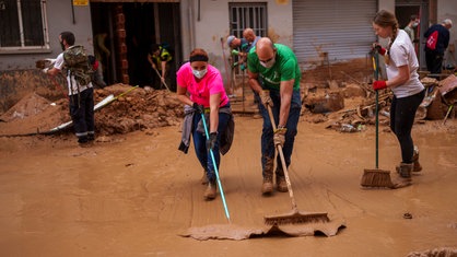 Menschen schaufeln Schlamm weg auf einer Straße in Valencia nach dem schweren Unwetter in Spanien