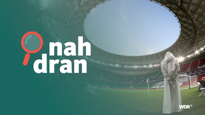 Mann mit traditioneller Kleidung steht in Fuball-Stadion in Katar. Daneben das Podcast-Logo: Schriftzug "nah dran", daneben eine kleine Lupe.