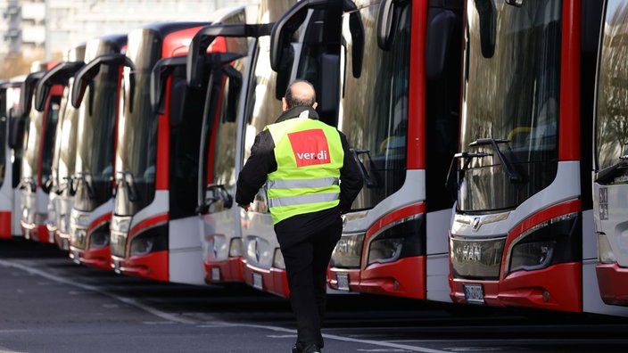 Geparkte Busse in einem Depot in Bonn. Davor ein Mann in einer Verdi-Warnweste