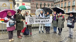 Die "Omas gegen Rechts" halten ihre Regenschirme und ein Banner mit der Aufschrift "Demokratie sichern, richtig wählen!"