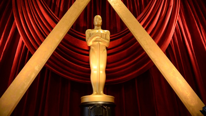 Goldene Oscar Statue vor rotem Vorhang.