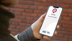 Eine Person mit Smartphone in der Hand, auf der die Palava-App geöffnet ist.