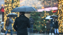 Mann mit Regenschirm läuft an Weihnachtsmarkt entlang