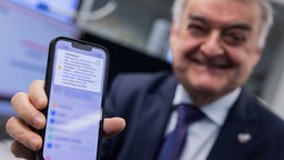 NRW Innenminister Reul zeigt sein Mobiltelefon. Es erscheint eine Cell Broadcast Warnmeldung. 