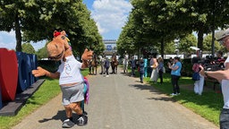 Pferde-Maskottchen mit Menschen und echten Pferden im Hintergrund