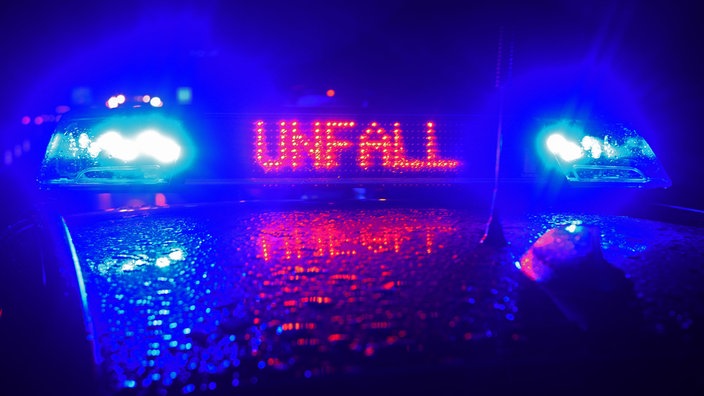 Ein Warnschild mit Aufschrift "Unfall" auf einem Polizeiauto im Regen.