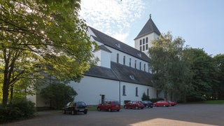 Außenansicht des Klostergebäudes mit parkenden Autos im Vordergrund