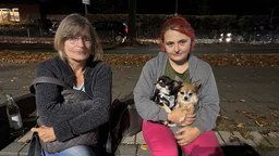 Zwei Frauen sitzen mit zwei Hunden auf einer Bank