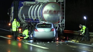 Ein silberner Pkw steht bei Nacht verunfallt vor einem großen Tanklaster auf der Autobahn. Drumherum befinden sich Polizisten mit Warnwesten.