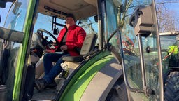 Ein Landwirt sitzt in seinem Traktor, man sieht ihn von leichter Entfernung.