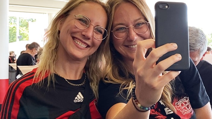 Zwei Frauen in Trikos von Bayer Leverkusen mach ein Foto von sich selbst im Stadion.