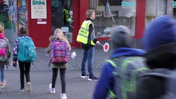 Tom Boddenberg steht auf der Straße vor einem Auto und lässt Kinder passieren