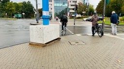 Ein Betonklotz auf dem ein blauer Metallpfeiler steht. Darauf klebt ein Plakat mit dem Text: Ist das Kunst oder kann das weg?