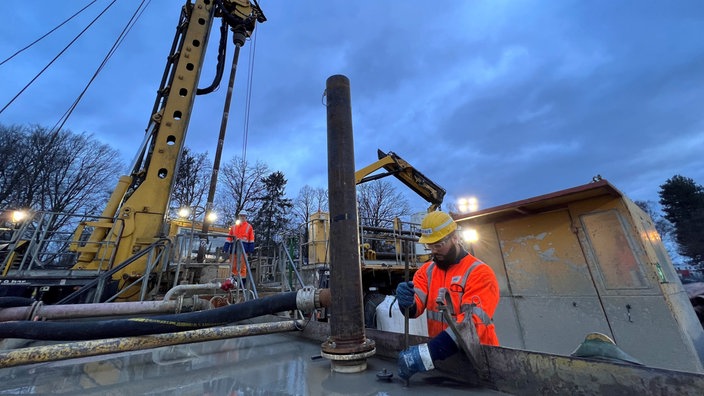 Ein Arbeiter steht in der Morgendämmerung an einem Arbeitsgerät und arbeitet